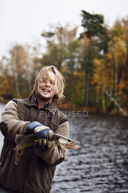 Young man holding fish, focus on foreground — Stock Photo