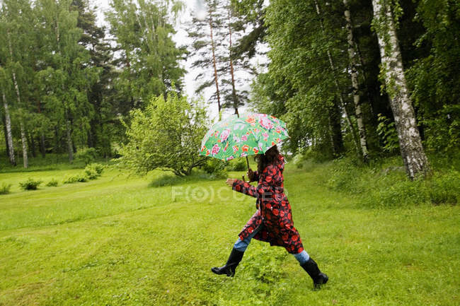 Frau in geflecktem Regenmantel läuft auf Feld — Stockfoto