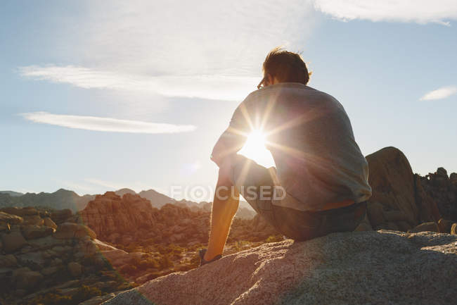 Homem sentado na rocha no Parque Nacional Joshua Tree e assistindo pôr do sol — Fotografia de Stock