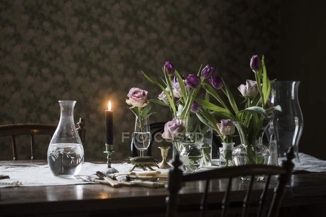 Mesa de madeira com vela acesa e vasos com flores — Fotografia de Stock