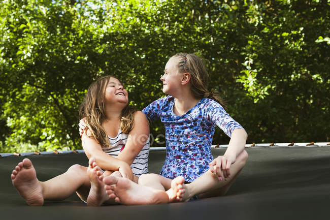 Deux filles assises sur le trampoline le jour ensoleillé — Photo de stock