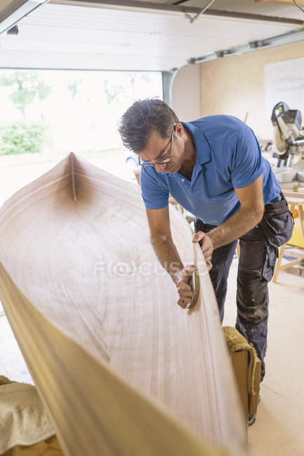 Man building wooden rowboat indoors — Stock Photo