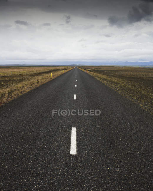 Road stretching through dry landscape under cloudy sky — Stock Photo