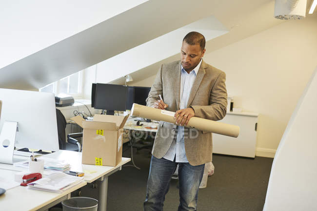 Empresário escrevendo nota sobre tubo de papel no escritório — Fotografia de Stock
