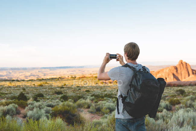 Vista trasera del hombre en el Parque Nacional Arches fotografiando paisaje - foto de stock