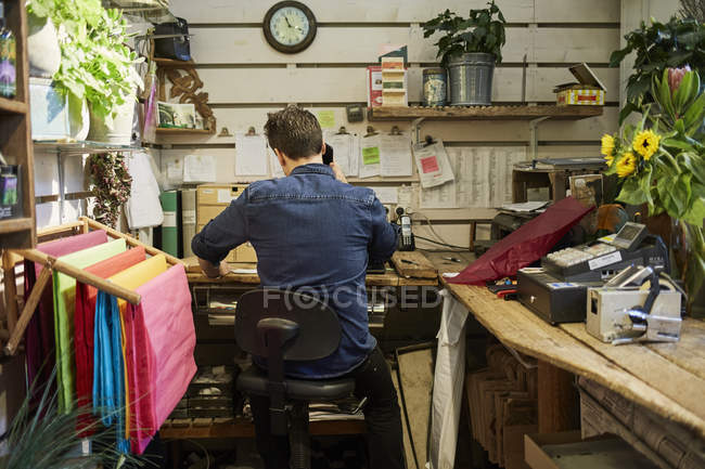 Vista posteriore del fiorista utilizzando il telefono nel negozio di fiori — Foto stock