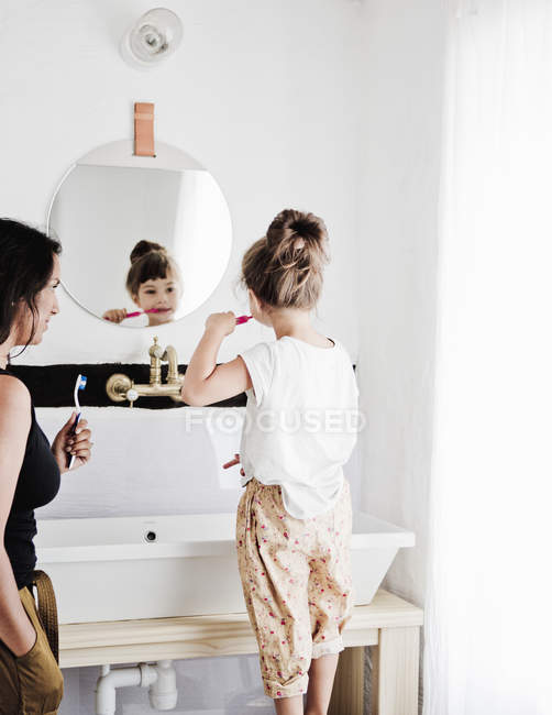 Madre e hija cepillando dientes en el baño - foto de stock