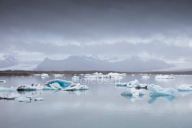 Floes de gelo no lago Jokulsarlon com gama de montanhas cobertas de neve no horizonte — Fotografia de Stock