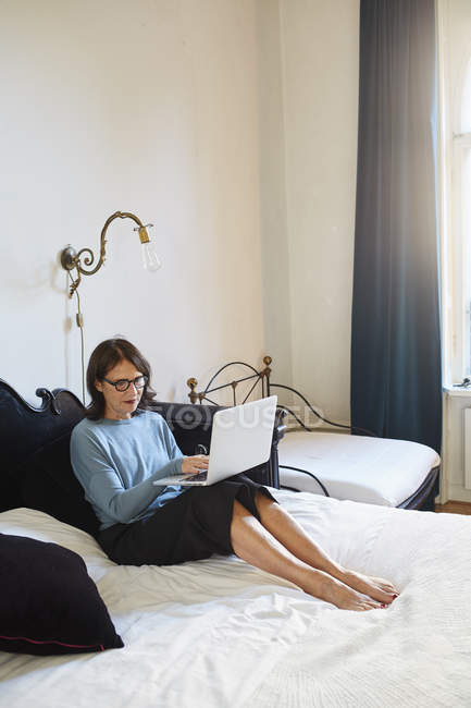 Donna seduta sul letto e utilizzando il computer portatile — Foto stock