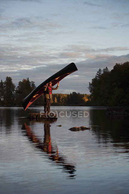 Homem de pé sobre pedra no lago segurando canoa — Fotografia de Stock