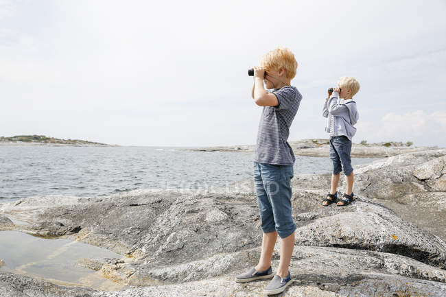 Two boys looking through binoculars on rocky seashore in Stockholm archipelago — Stock Photo