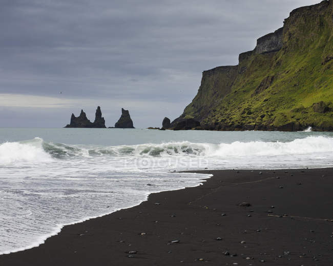 Скельні утворення та чорний пісок на пляжі за скелею — стокове фото