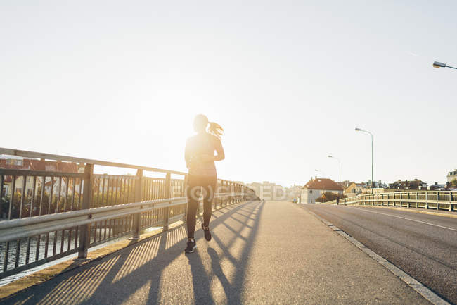 Joven mujer corriendo en puente en retroiluminación - foto de stock