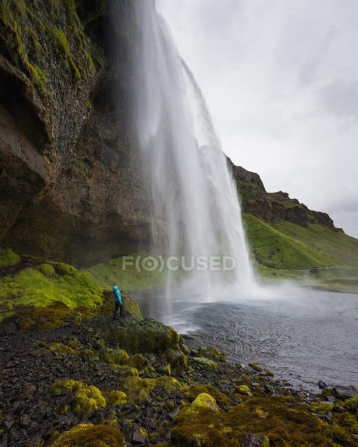 Hiker looking up at Seljalandsfoss waterfall, blurred motion — Stock Photo