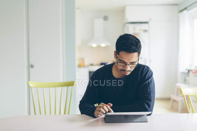 Homem adulto médio sentado à mesa na sala de jantar e usando tablet — Fotografia de Stock