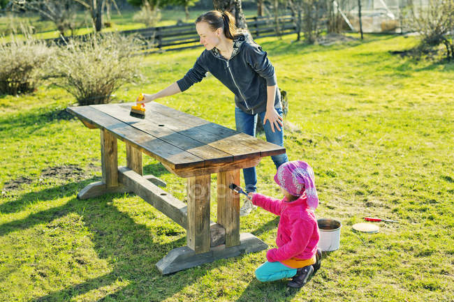 Mother with daughter oiling wooden table in garden — Stock Photo
