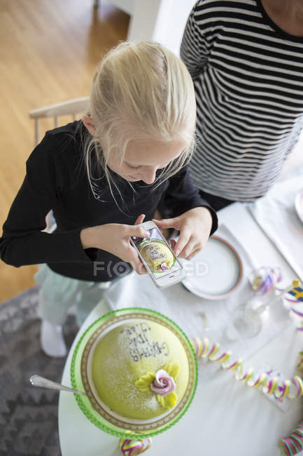Girl photographing birthday cake with cell phone — Stock Photo