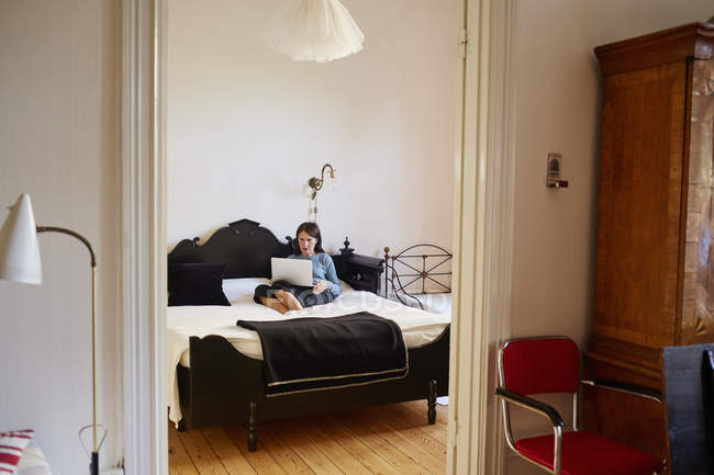 Жінка використовує ноутбук на ліжку, вид через дверний отвір — стокове фото