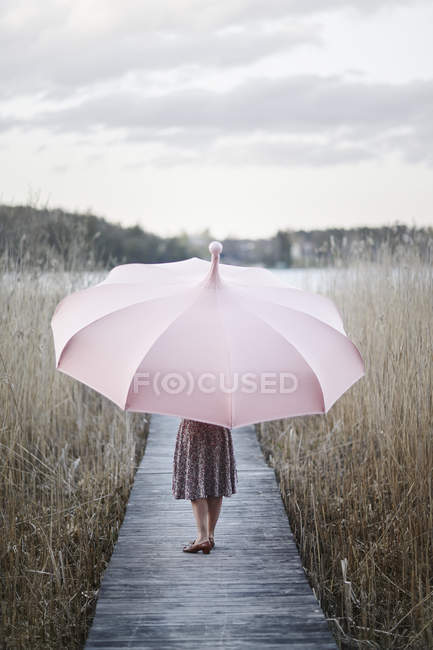 Mulher com guarda-chuva rosa em pé no cais de madeira — Fotografia de Stock