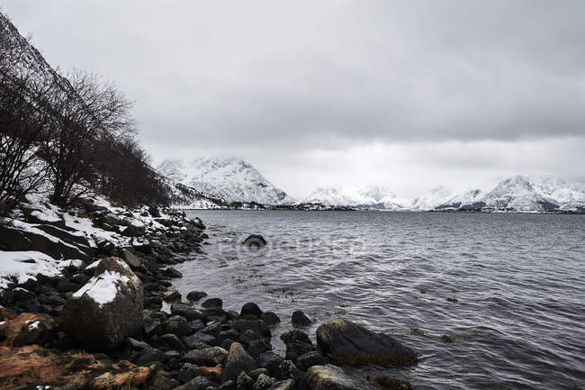 Rocky river shore and snow covered mountains — Stock Photo