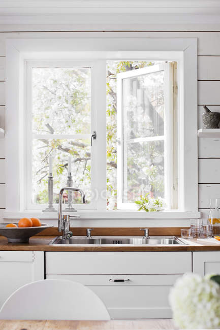 Évier par fenêtre blanche dans la cuisine domestique — Photo de stock