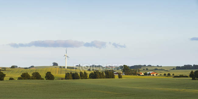 Vista panorâmica de campos verdes com turbina eólica sob céu azul — Fotografia de Stock