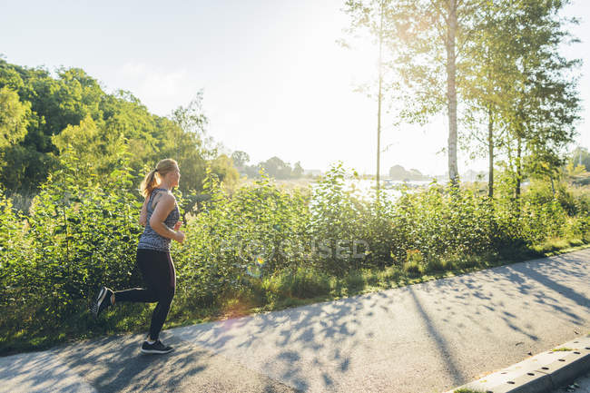 Молода жінка біжить на тротуарі на сонячному світлі — стокове фото