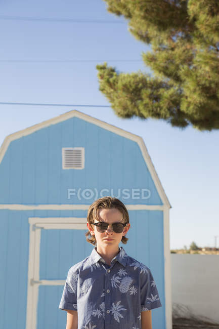 Garçon portant des lunettes de soleil debout devant la grange bleue — Photo de stock