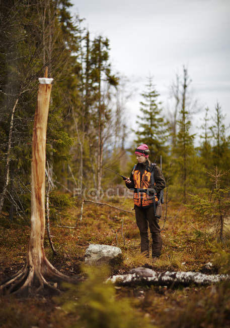 Chasseur féminin utilisant le téléphone satellite dans la forêt — Photo de stock