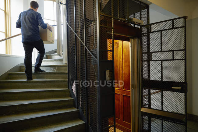 Mann geht auf Stufen, trägt Kiste — Stockfoto