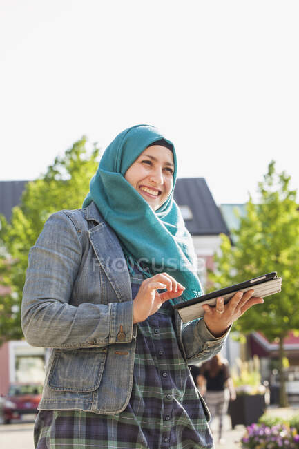 Mujer musulmana usando tableta y sonriendo Archivo de liberación roto - foto de stock