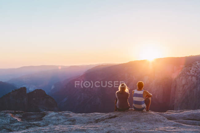 Hombre y mujer observando la puesta de sol en las montañas en el Parque Nacional Yosemite - foto de stock
