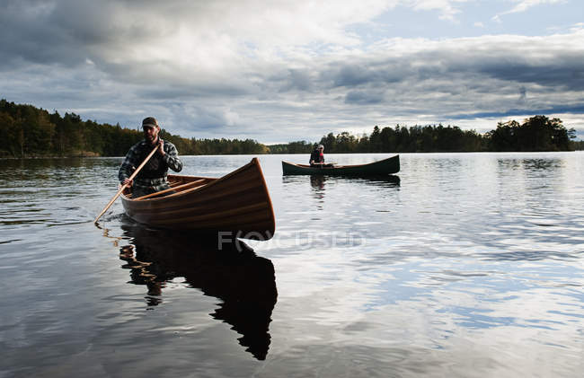 Hombres remando canoas en el lago bajo el cielo con nubes - foto de stock
