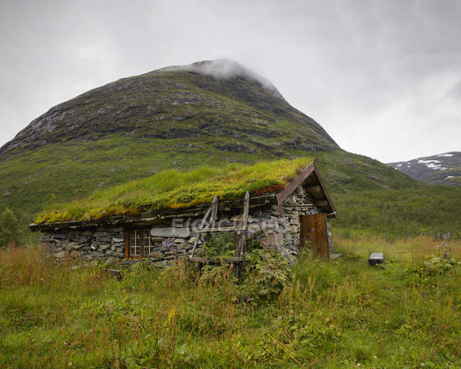 Stone hut with grassy roof under green mountain — Stock Photo