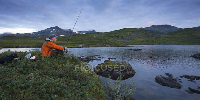 Vue latérale de l'homme pêche dans le lac Sjuendevatnet au crépuscule — Photo de stock