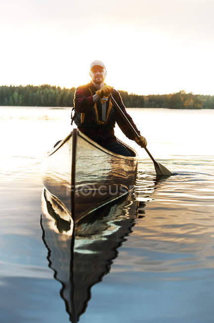 Человек в бейсболке катается на каноэ на озере — стоковое фото