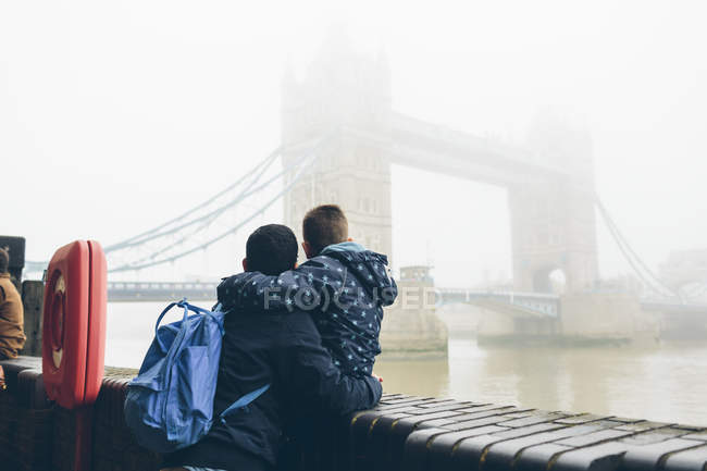 Homem adulto médio segurando menino enquanto olha para Tower Bridge em Londres no nevoeiro — Fotografia de Stock