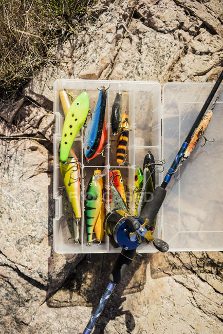 Box of fishing tackles and fishing rod on rock — Stock Photo