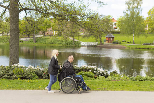 Человек в инвалидной коляске с личным ассистентом в парке — стоковое фото