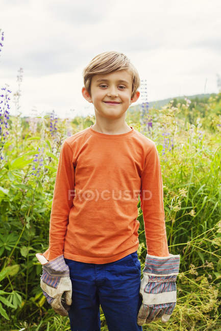 Boy wearing work gloves against meadow — Stock Photo