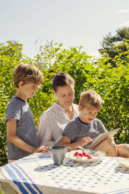 Изображение двух сыновей и матери, использующих цифровой планшет в саду — стоковое фото