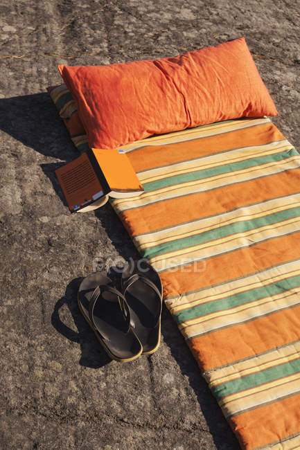 Erhöhter Blick auf orangefarbene Matratzen, Flip Flops und Buch im Sommer — Stockfoto
