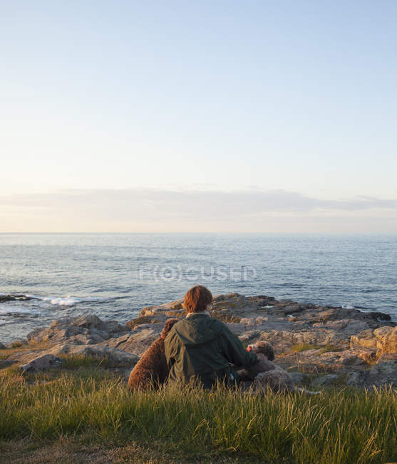 Mature woman with dogs sitting on rocky coastline at Bornholm, Denmark — Stock Photo