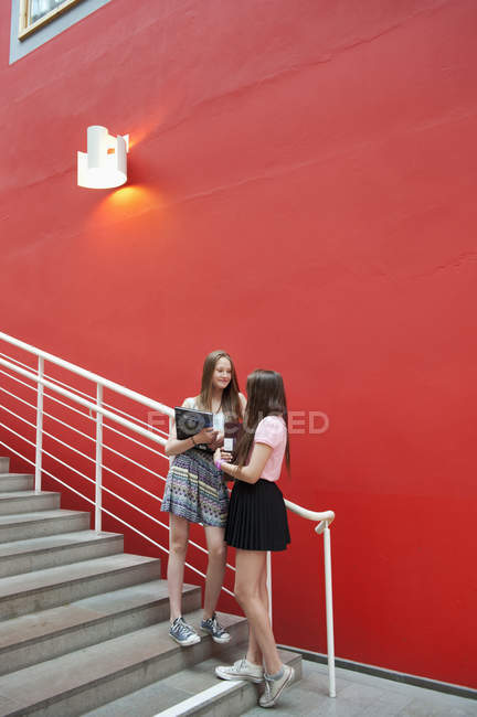 Teenage girls talking outside school against red wall — Stock Photo