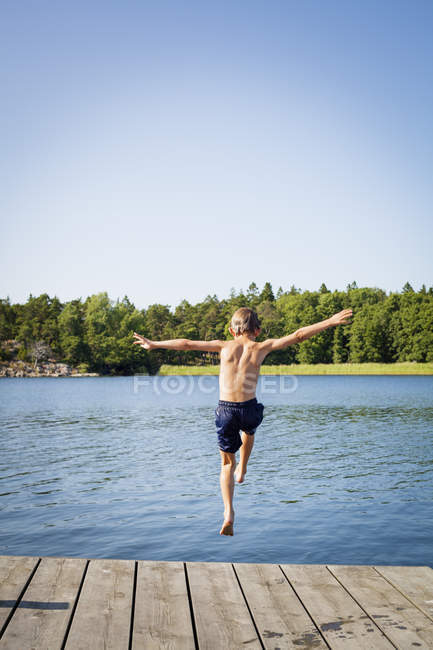 Rückansicht eines Jungen, der von Steg ins Wasser springt — Stockfoto