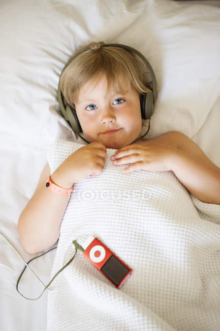 Retrato de menina loira usando fones de ouvido enquanto deitada na cama — Fotografia de Stock