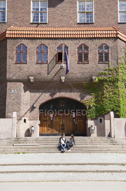 Estudiantes sentados en escaleras frente al edificio de la escuela - foto de stock