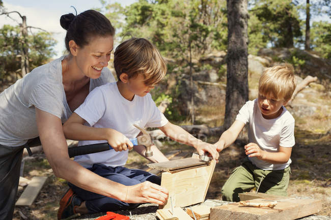 Mother helping sons to build birdhouse — Stock Photo