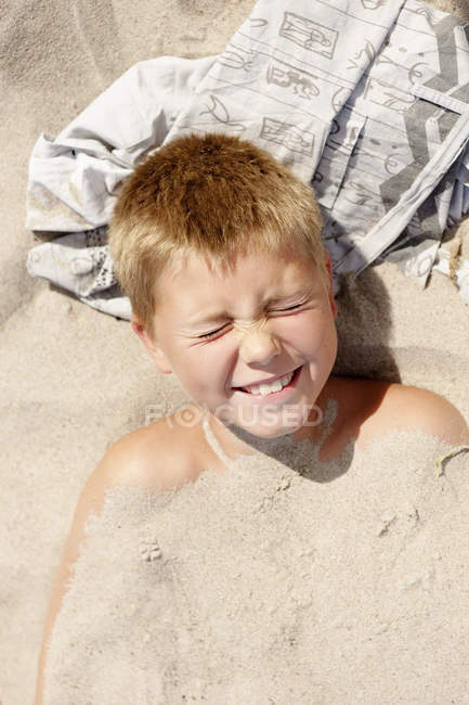 Niño con los ojos cerrados yaciendo en la arena - foto de stock