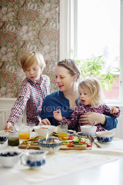 Madre con dos hijos desayunando en el comedor - foto de stock